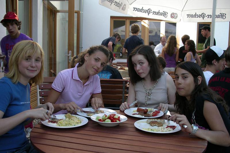 Amigas están sentadas en una mesa bajo una sombrilla mientras comen en el comedor de curso verano alemania