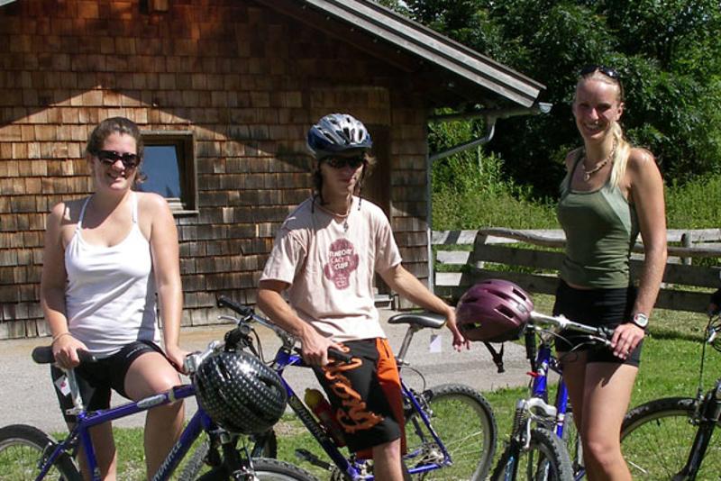 Tres campistas con bicicleta y cascos bajo el sol en el césped junto al albergue de curso verano alemania