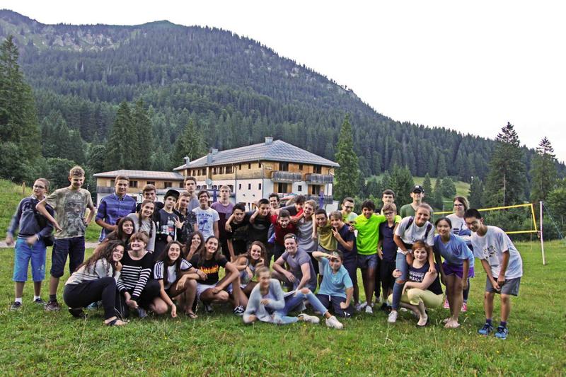 Grupo grande de campistas posan juntos en el césped cerca de las instalaciones del campamento con la montaña de fondo en curso de idiomas en alemania