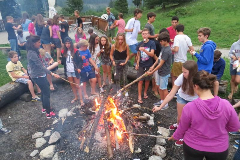 Campers alrededor del fuego con palos tostando nubes de azúcar y comiendo en curso verano alemania