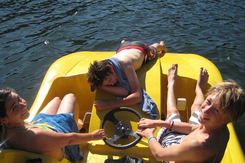 Tres campers toman el sol en lancha a pedales en el agua mientras sonríen en curso de aleman alemania