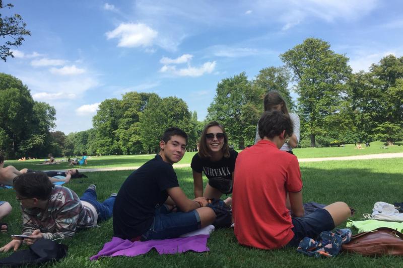 Campers descansan y charlan sobre toallas en la sombra de los árboles en una pradera de curso de aleman en alemania 