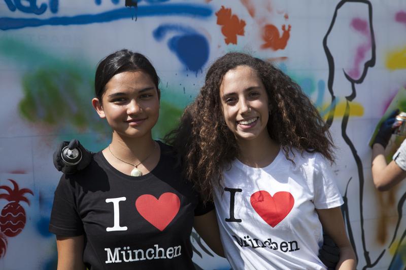 Dos amigas posan con camisetas a juego mientras pintan una pared con spray de pintura en curso de aleman alemania
