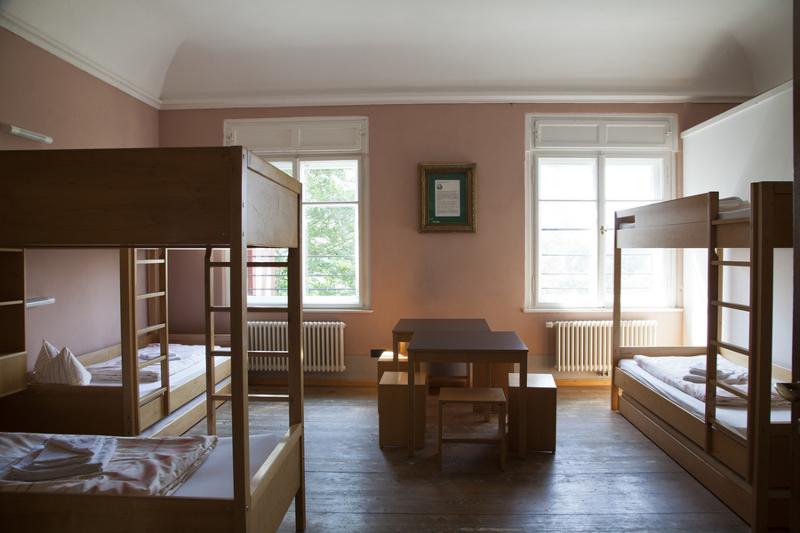 Habitación compartida con tres literas y mesas con bancos y ventanas en curso 