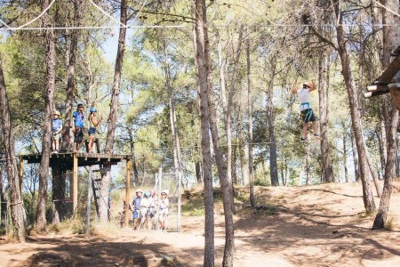 una foto de un bosque con niños jugando en un campamento multiaventura