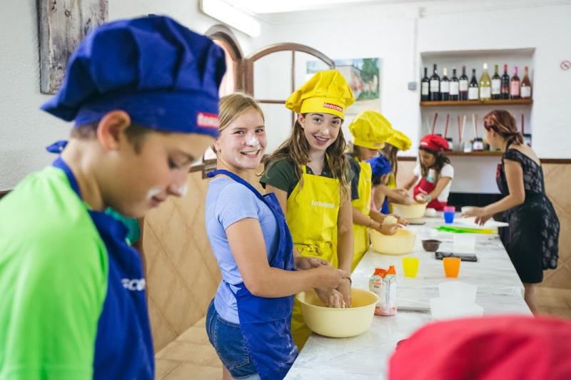 un grupo de niños mirando a camara en una clase de cocina en un campamento de cocina
