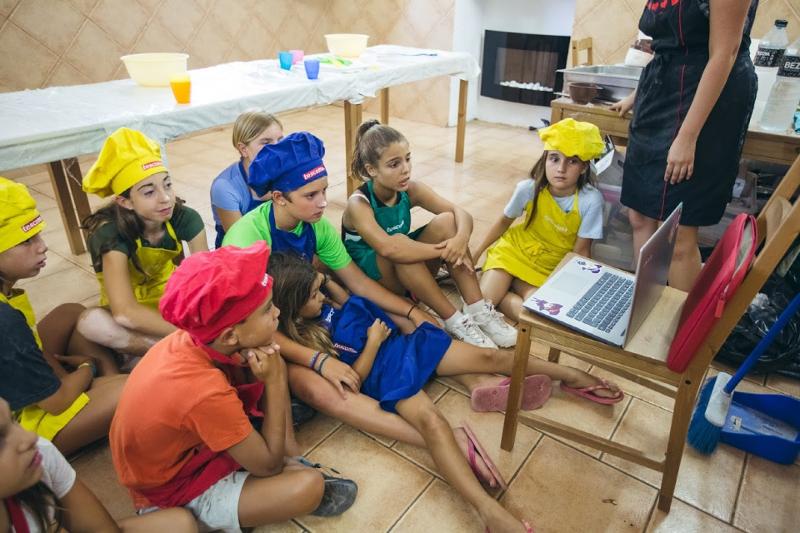 Un grupo de niños en una clase de cocina mirando un ordenador portátil en un  campamento de verano en barcelona 