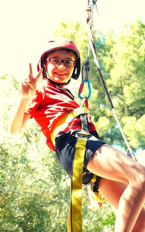 un niño sonriendo a camara en una tirolina de un campamento cazorla