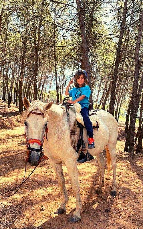 una niña montada a caballo en un bosque en un campamento de verano jaen