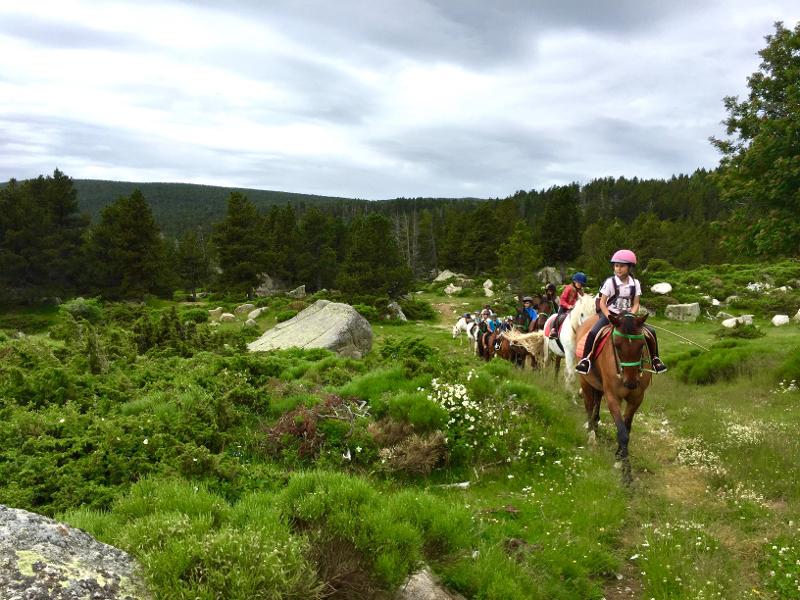 una foto de un grupo de niños montando a caballo en una pradera de un campamentos en pirineos