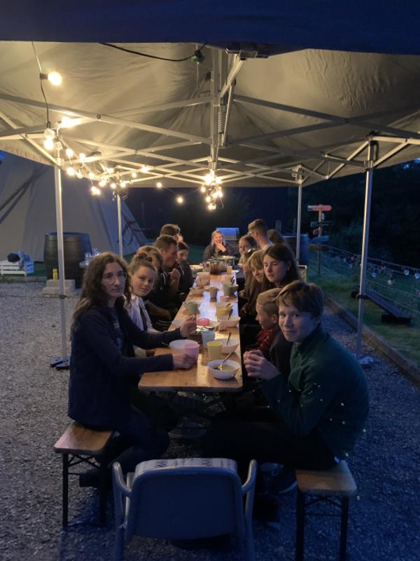 Jóvenes cenando todos juntos en una mesa larga al aire libre en el campamento en irlanda