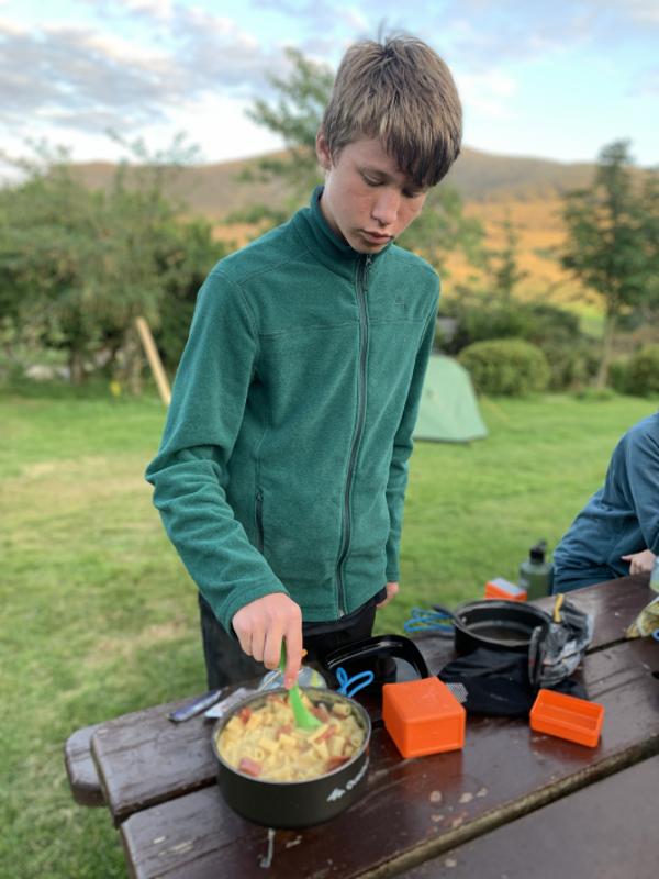 Niño cocinando en una pequeña olla al aire libre en el campamento irlanda