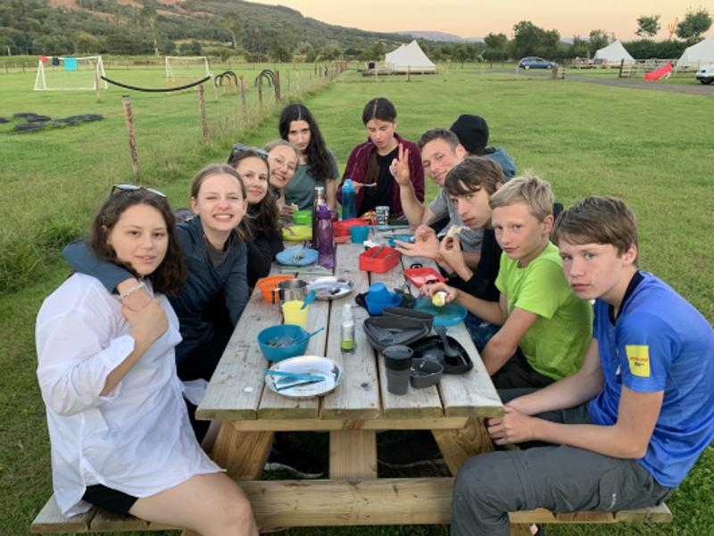 Jóvenes comiendo en una mesa de picnic al aire libre en el campamento irlanda