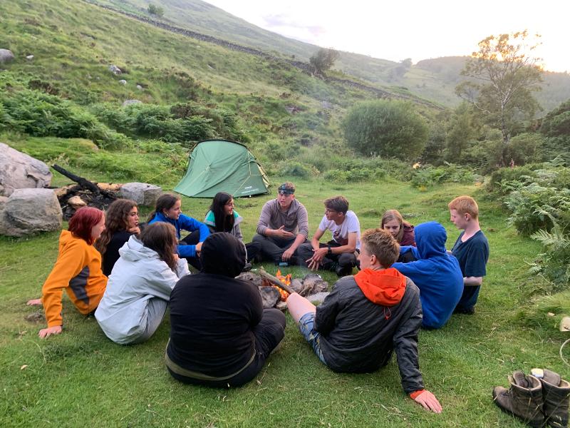 Jóvenes sentados alrededor de una hoguera en la montaña en el campamento ingles irlanda 