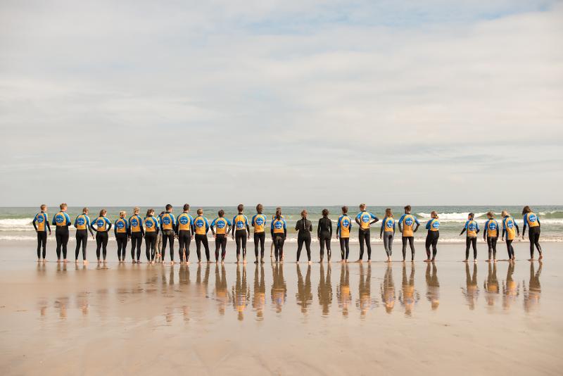 Foto grupal de los jóvenes en el campamento de verano irlanda de pie con sus neoprenos mirando el mar en la playa
