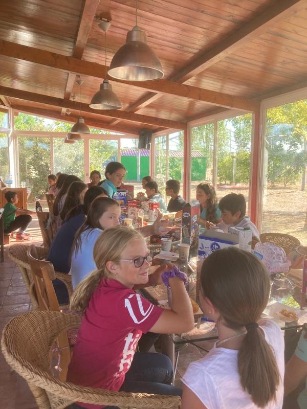 Niños comiendo juntos en una mesa larga en un campamento de verano
