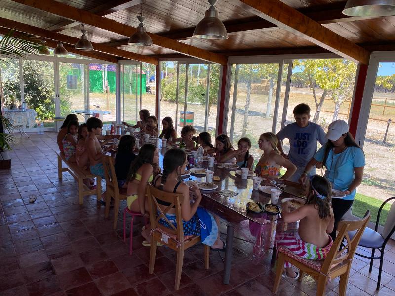 Niños y niñas comiendo en una mesa larga en un campamento para niños