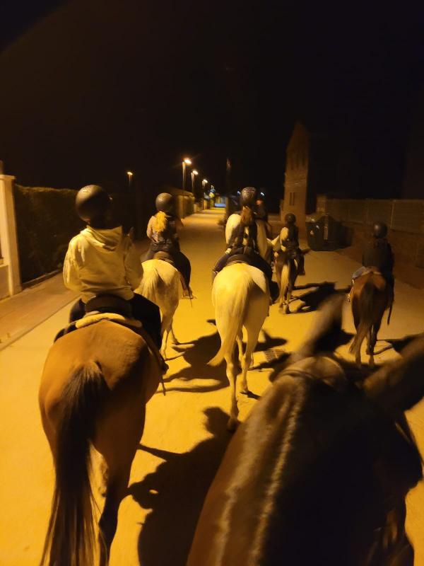 Niños y niñas dando un paseo nocturno con sus caballos en un campamento para niños