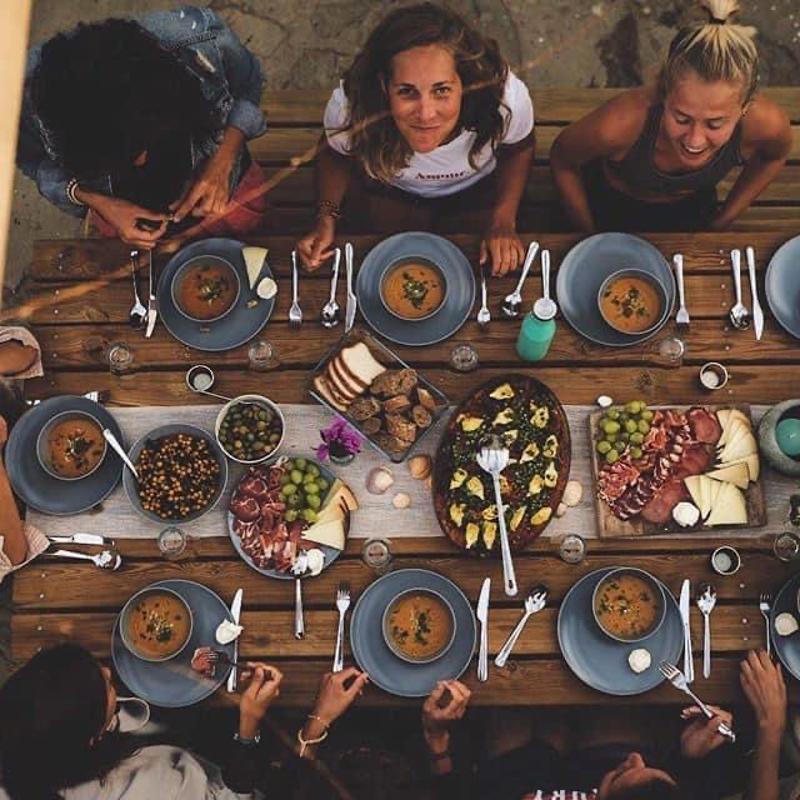 Una foto hecha desde arriba en la que se ve un grupo de jovenes comiendo en una mesa grande de madera en un campamento cadiz