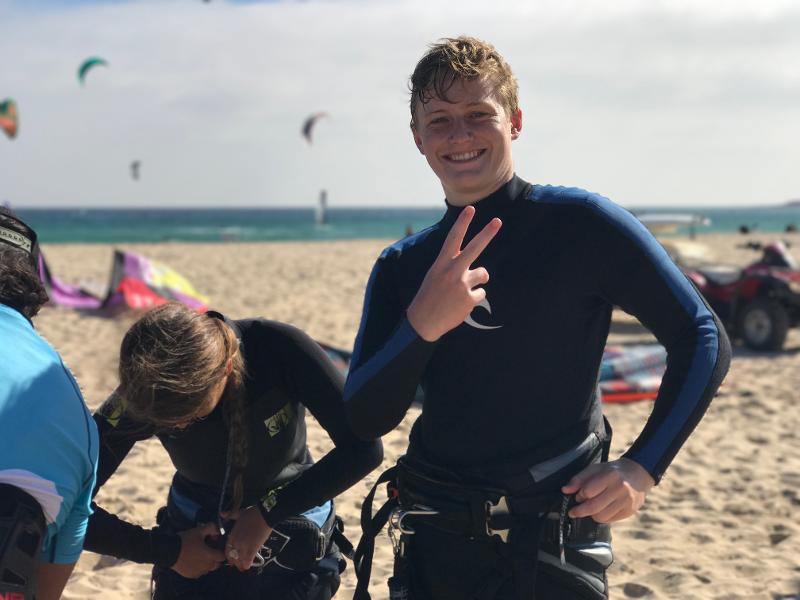 Un chico sonriendo a cámara en una playa en un campamento kitesurf