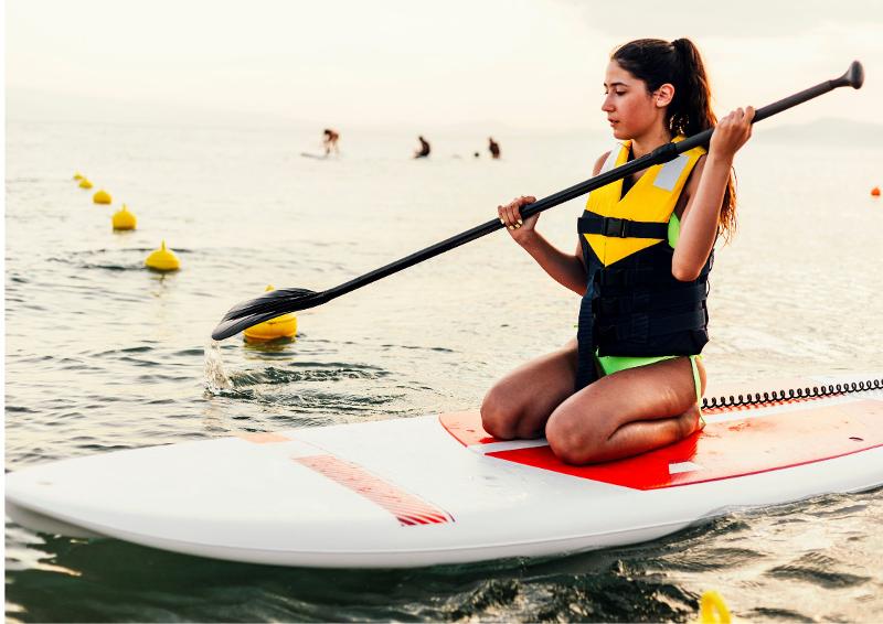 Una joven encima de una tabla de paddle surf en un campamento multideporte