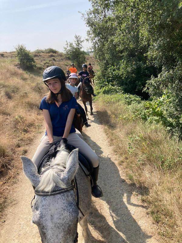 un grupo de niños en fila montados a caballo en un campamento de caballos
