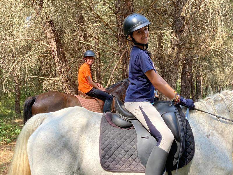 Dos niños montando a caballo mirando a camara en un campamento de caballos