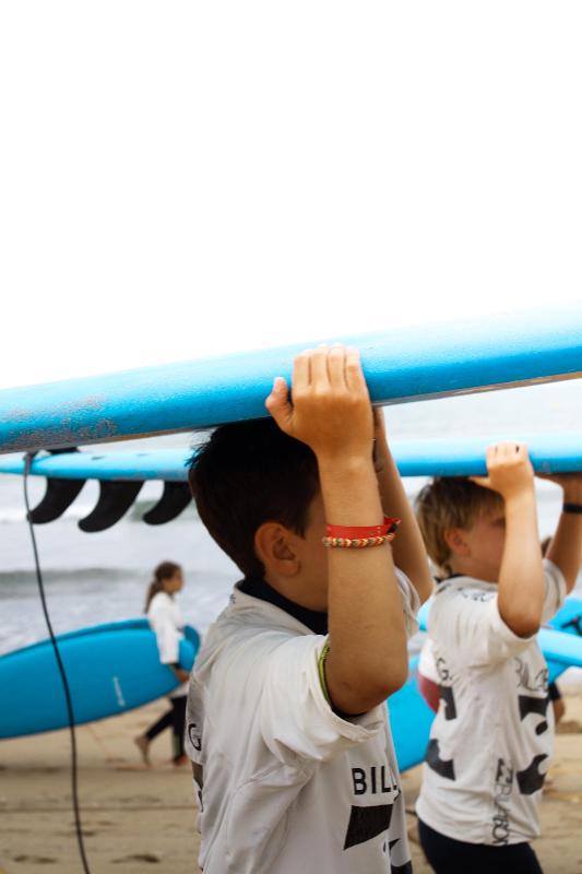 Niños llevando tablas de surf en un surf camp pais vasco