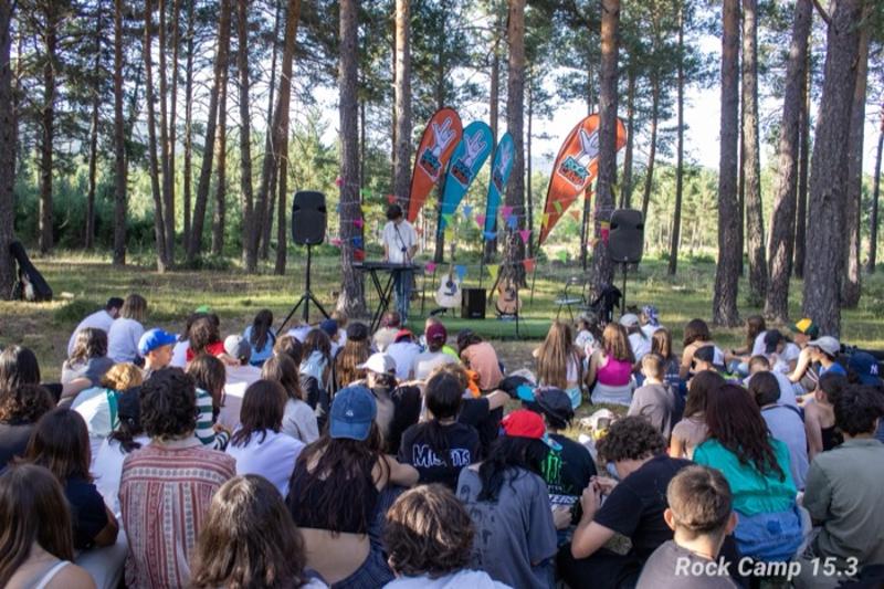 Una foto de un grupo de personas mirando a alguien tocar instrumentos en un campamento de musica en verano