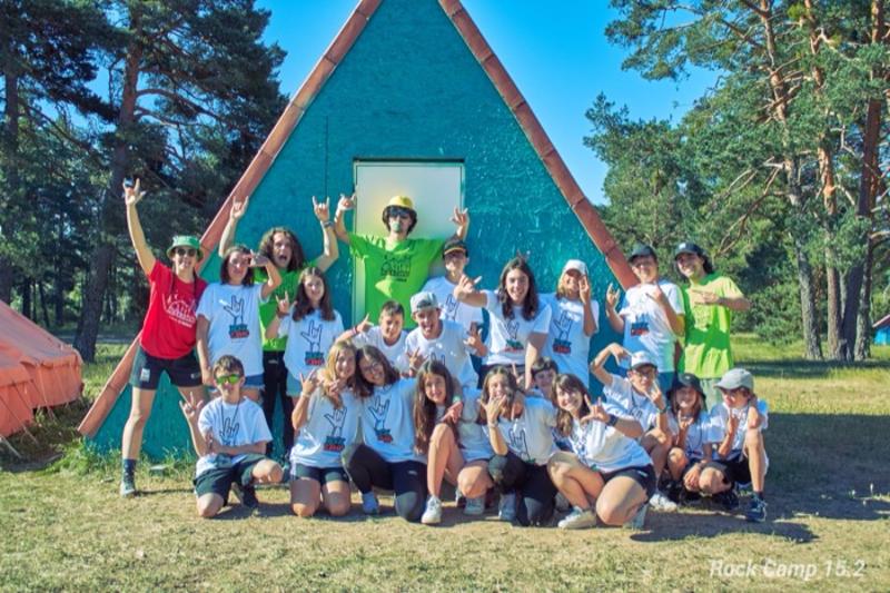 Un grupo de jovenes en frente de una cabaña de un campamento de verano musica