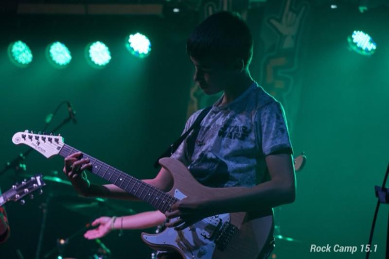 Un joven tocando al guitarra electrica en un campamento de verano musica