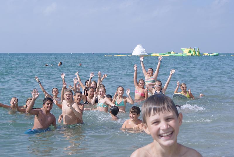 Un grupo de niños nadando en el mar sonriendo a camara en un campamento de verano en marbella