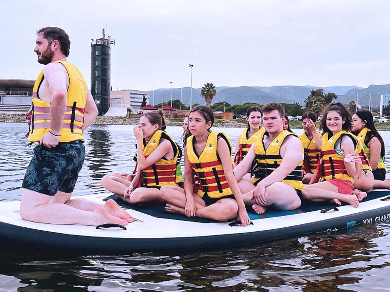 Un grupo de jovenes en una tabla grande en el agua en un summer camp barcelona
