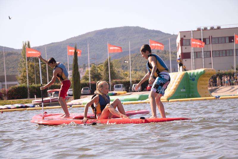 Tres niños practicando paddle surf en un campamento de verano