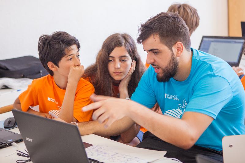 Monitor explicando a unos niños algunas aspectos de programación frente a un portátil durante un campamento robótica madrid