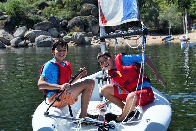 Dos niños felices montados en su barco de vela hinchable en las clases practicas del campamento vela